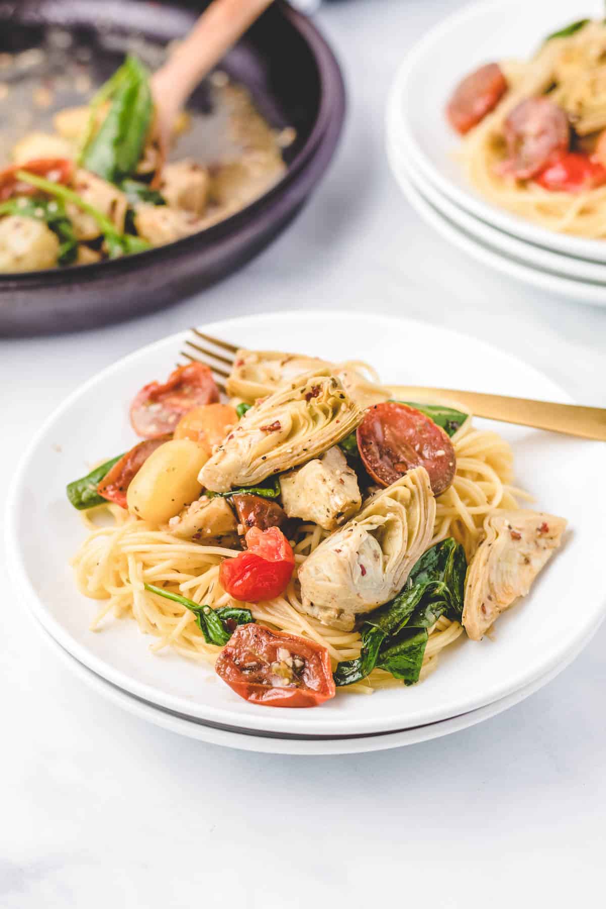 A bowl of spaghetti pasta topped with Italian artichokes, tomatoes, and spinach.