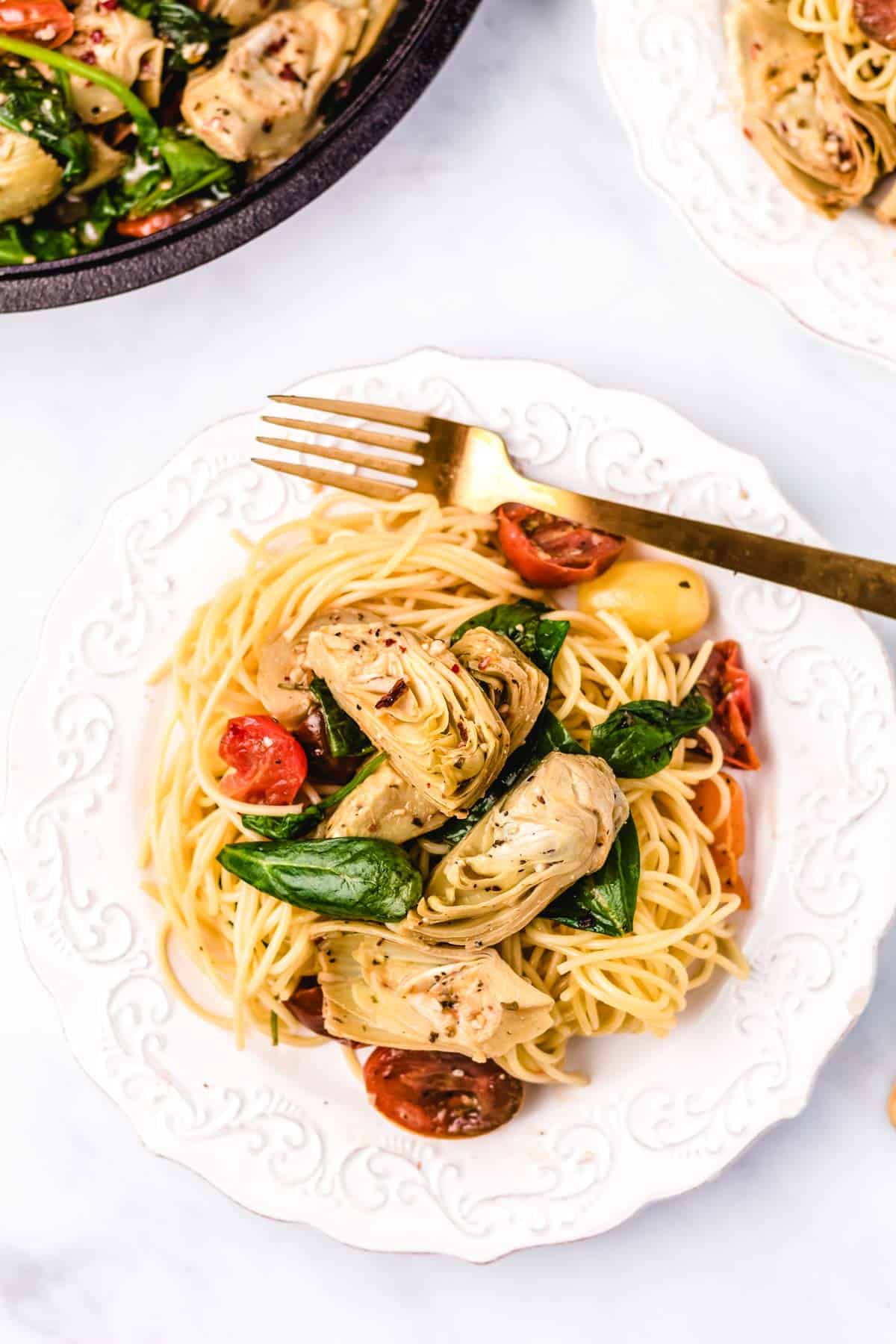 A white serving plate filled with pasta topping with Italian artichoke medley.