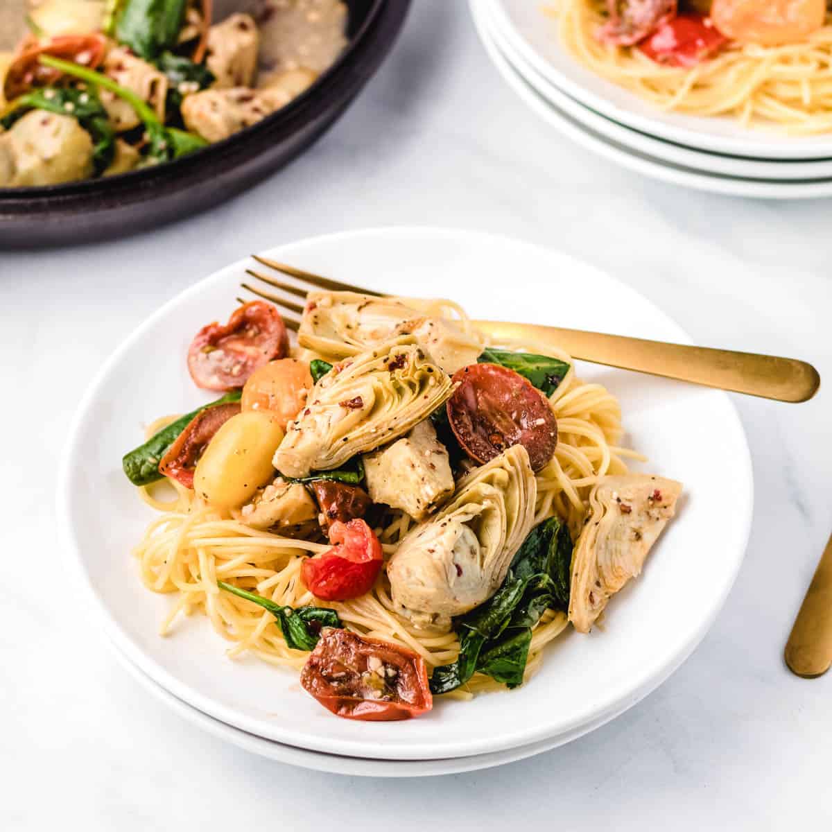 A plate of pasta with Italian artichoke hearts, cherry tomatoes, and spinach.