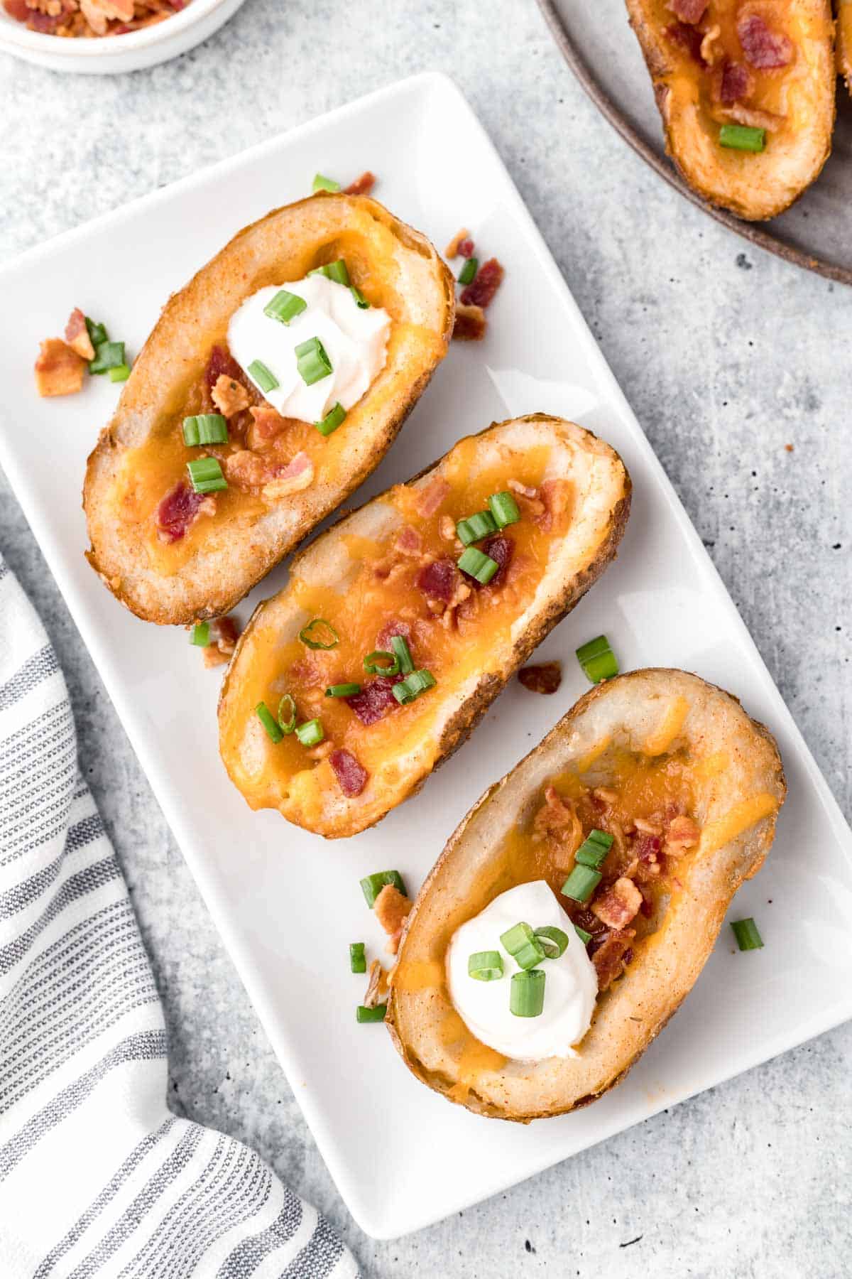 A white serving tray filled with potato skins on a marbled table with a gray and white tea towel to the side.