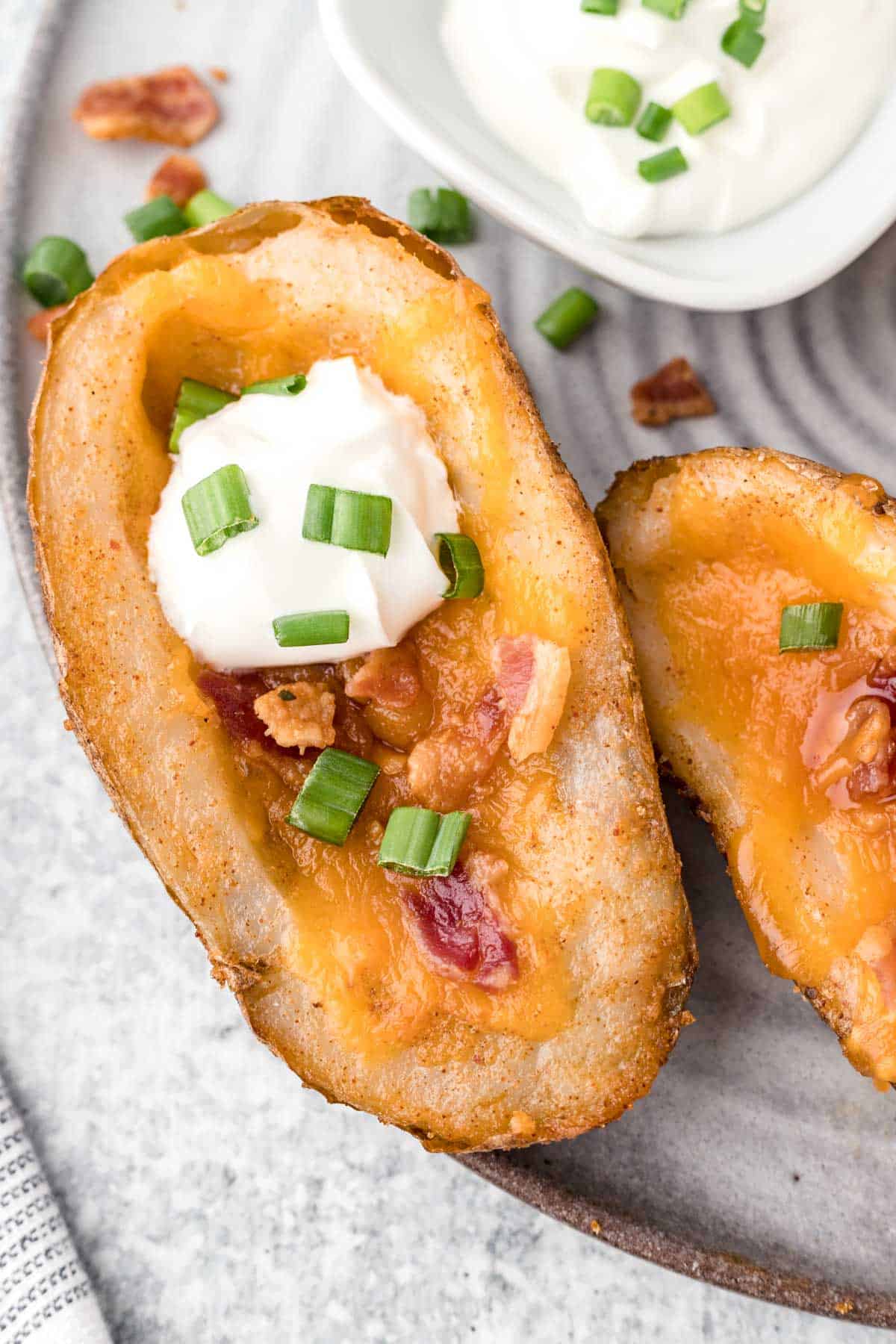 An up-close image of a baked potato skin layered with melted cheese, crispy bacon, sour cream, and sliced green onions.