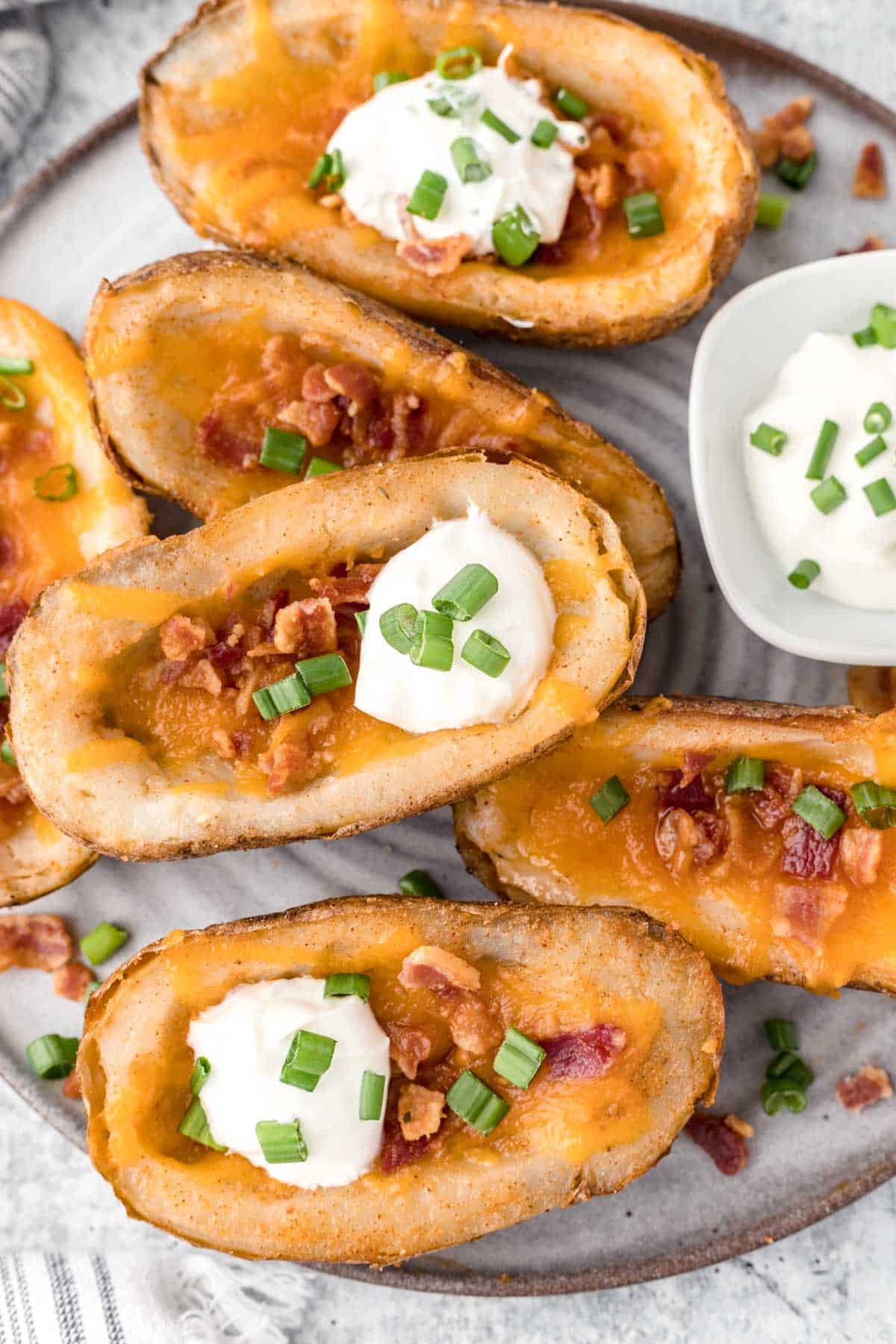 A plate full of loaded potato skins with sour cream for dipping.