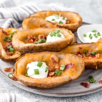 A plate filled with potato skins topped with melted cheddar cheese, crispy bacon, a dollop of sour cream and green onions.