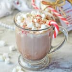 A cup of peppermint hot cocoa in a glass mug topped with crushed peppermints and mini marshmallows.