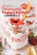 A handled mason jar glass willed with layers of Strawberry, yougurt and granola in this Strawberry Parfait.