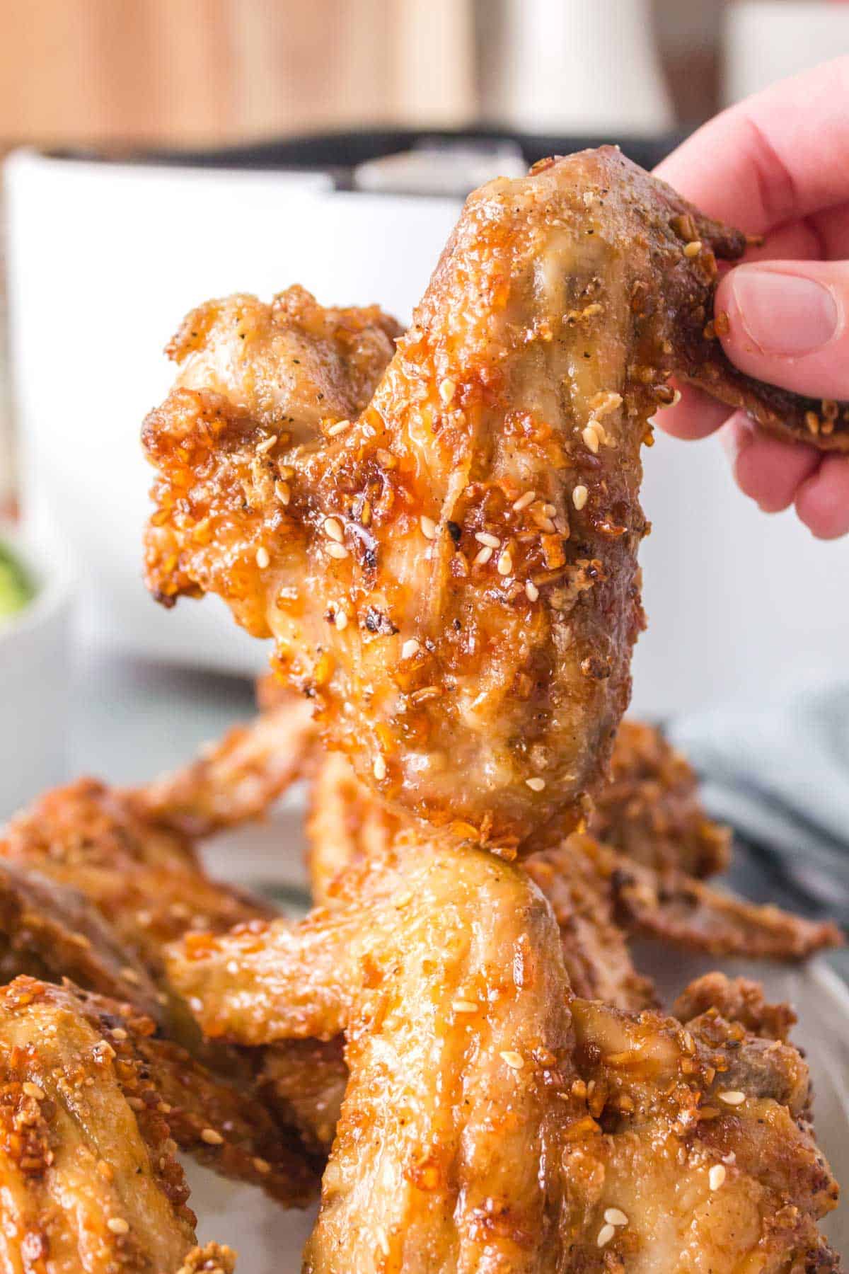 A hand lifting up a chicken wing from a plate of wings.