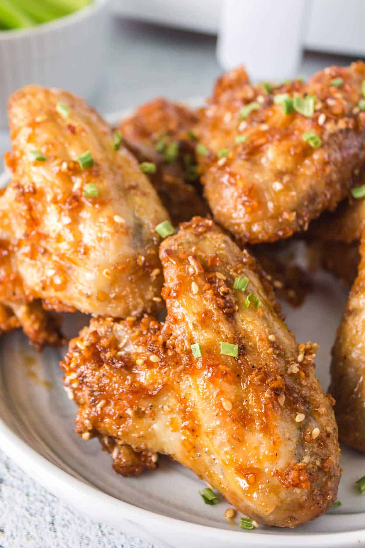 A white plate piled with air fryer honey garlic chicken wings garnished with chives.
