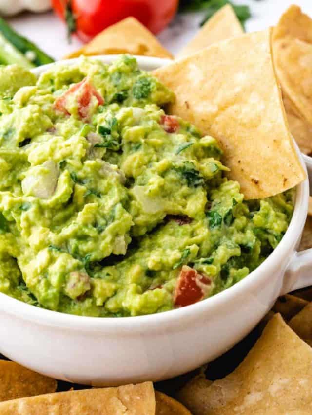 A white bowl filled with homemade guacamole with a chip dipped in it.