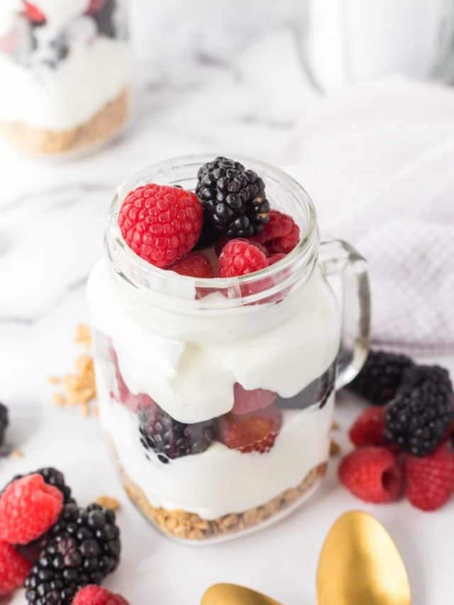 A Mason jar mug filled with a breakfast parfait made with granola, yogurt, and fresh fruit.