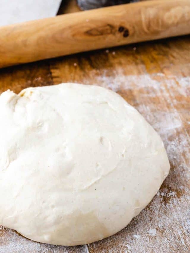 A no-rise pizza dough ball set on a floured wooden board.