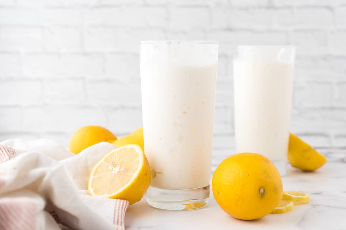 Two tall glasses filled with copycat chick-fil-a frosted lemonade with lemons and a tea towel.