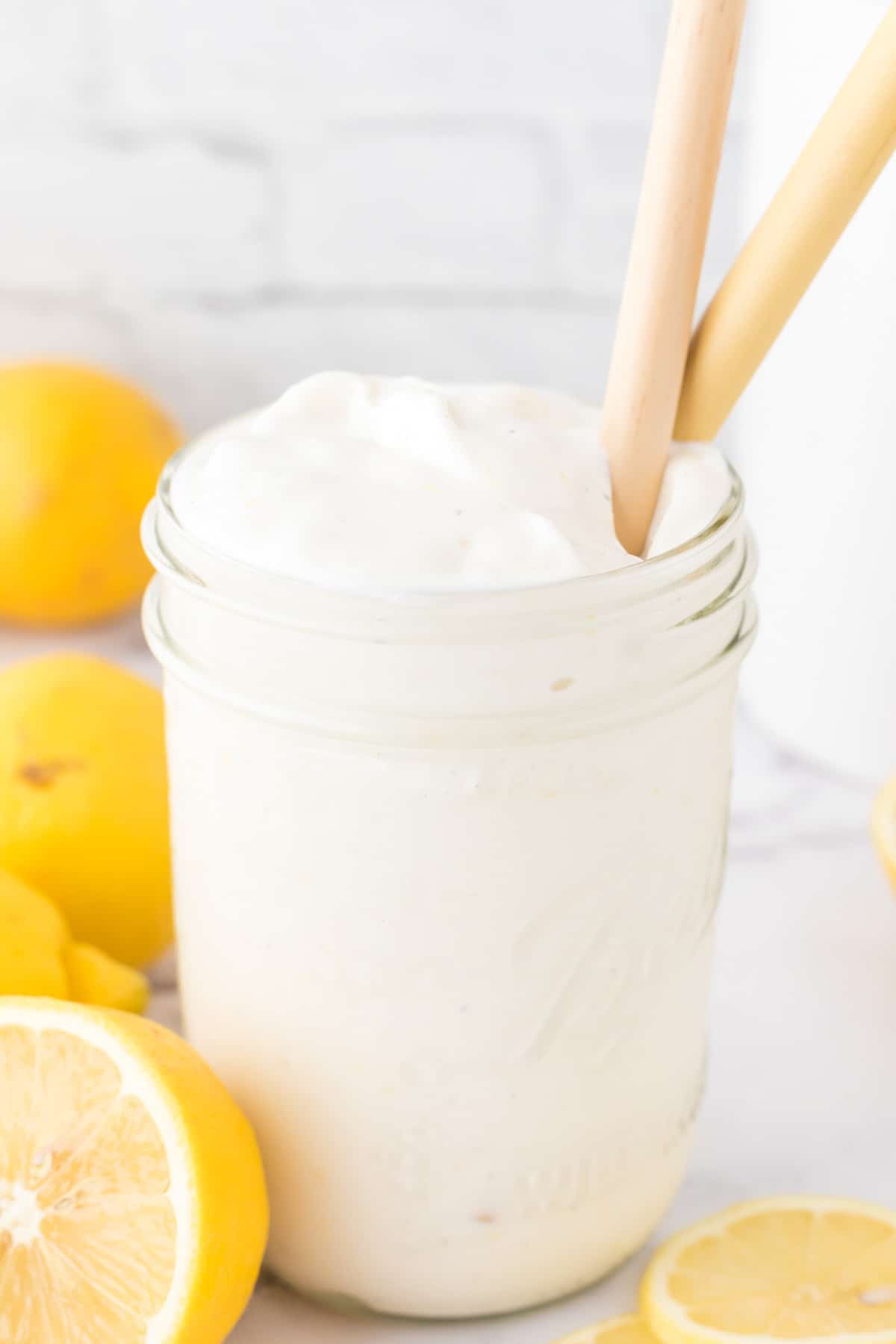 A mason jar full of frosty vanilla lemonade milkshake with two wooden spoons in the cup.