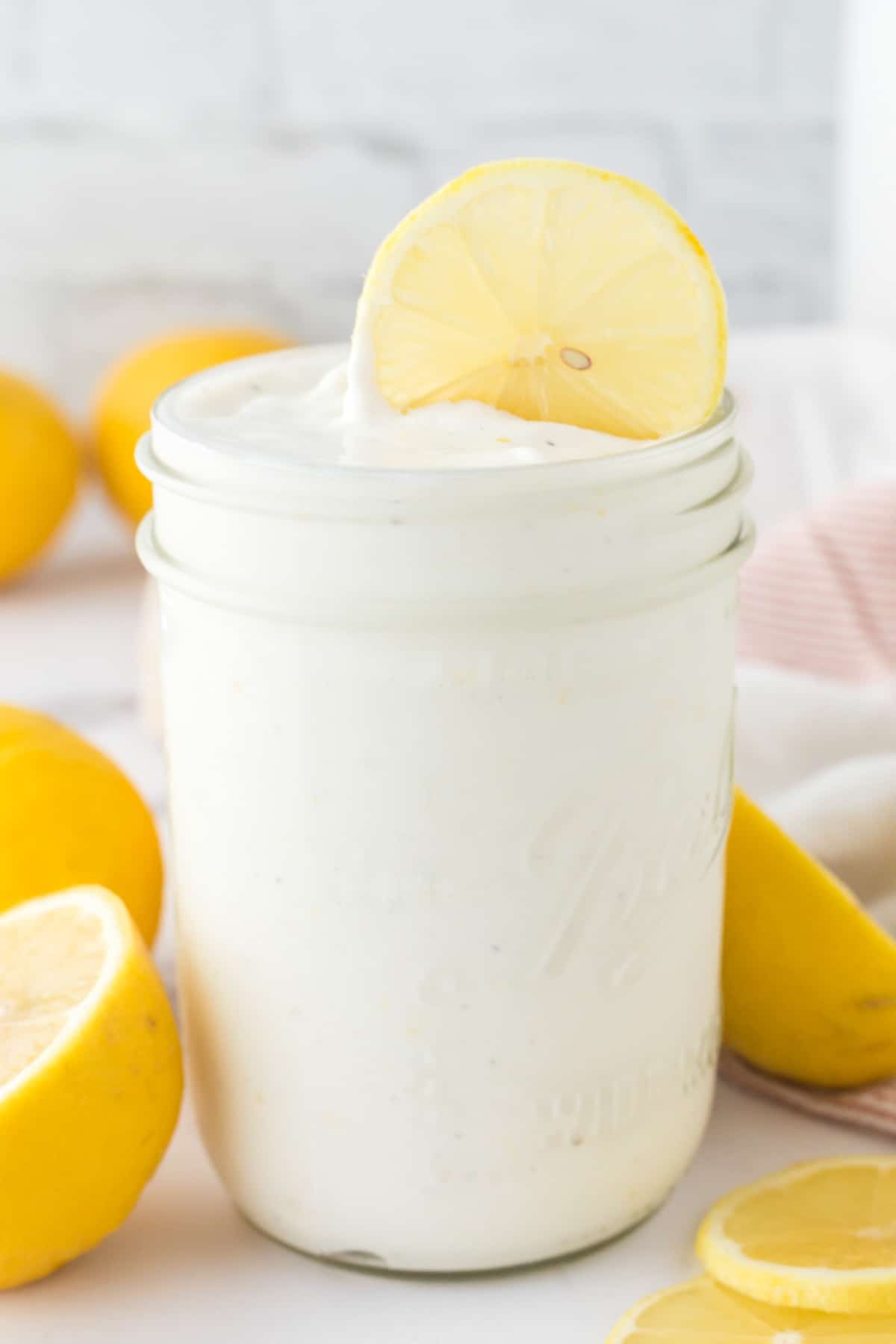 A mason jar will with creamy frosted lemonade topped with a lemon slice .
