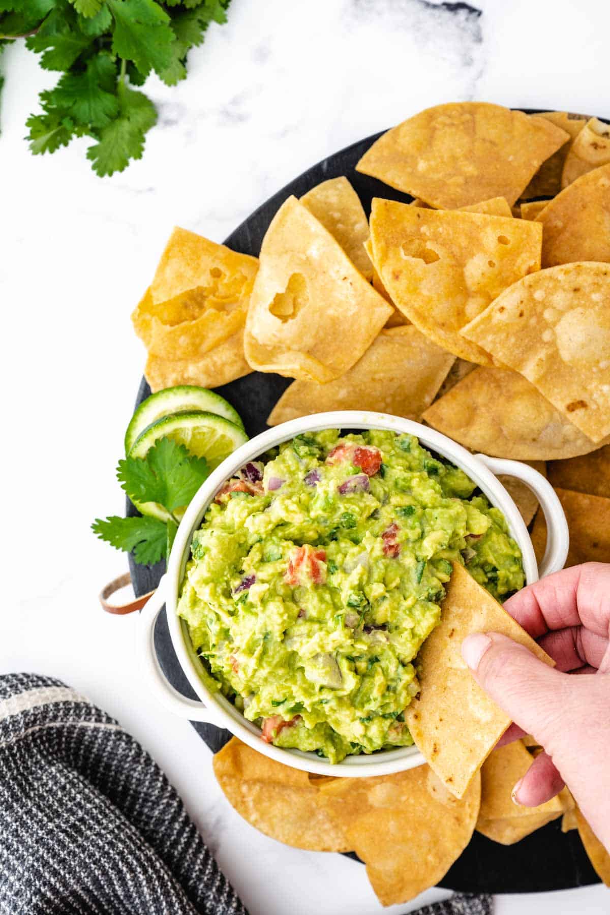 A hand dipping a tortilla chip into guacamole dip.