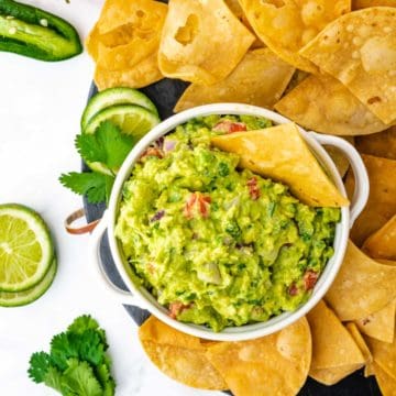 An overhead image of the best guacamole on a black serving tray with homemade tortilla chilps.