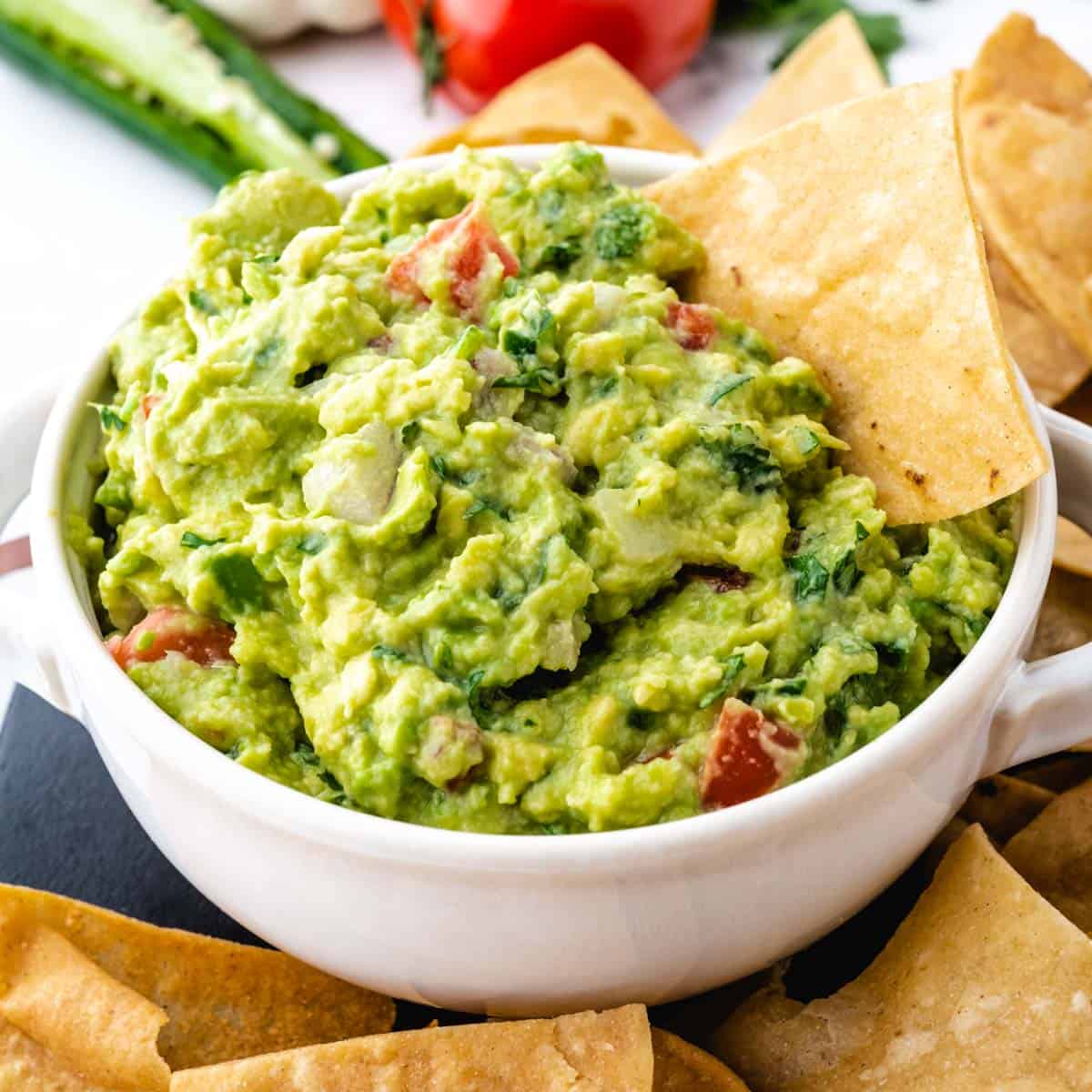 A white bowl filled with homemade guacamole with a chip dipped in it.