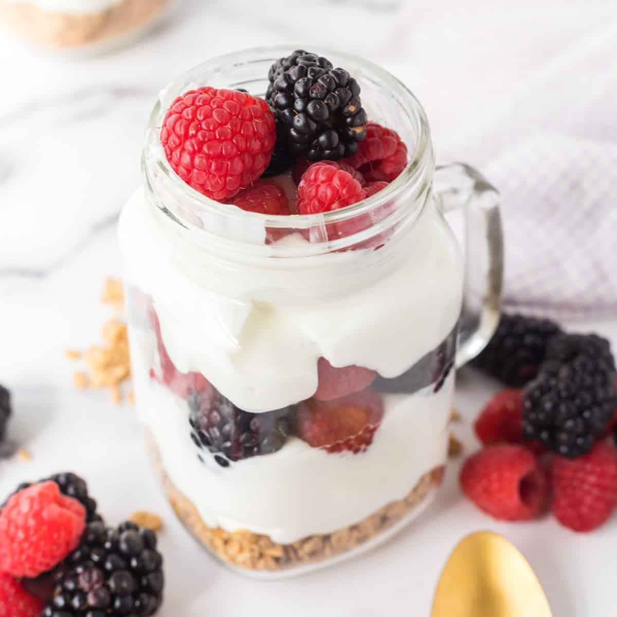 A Mason jar mug filled with a breakfast parfait made with granola, yogurt, and fresh fruit.