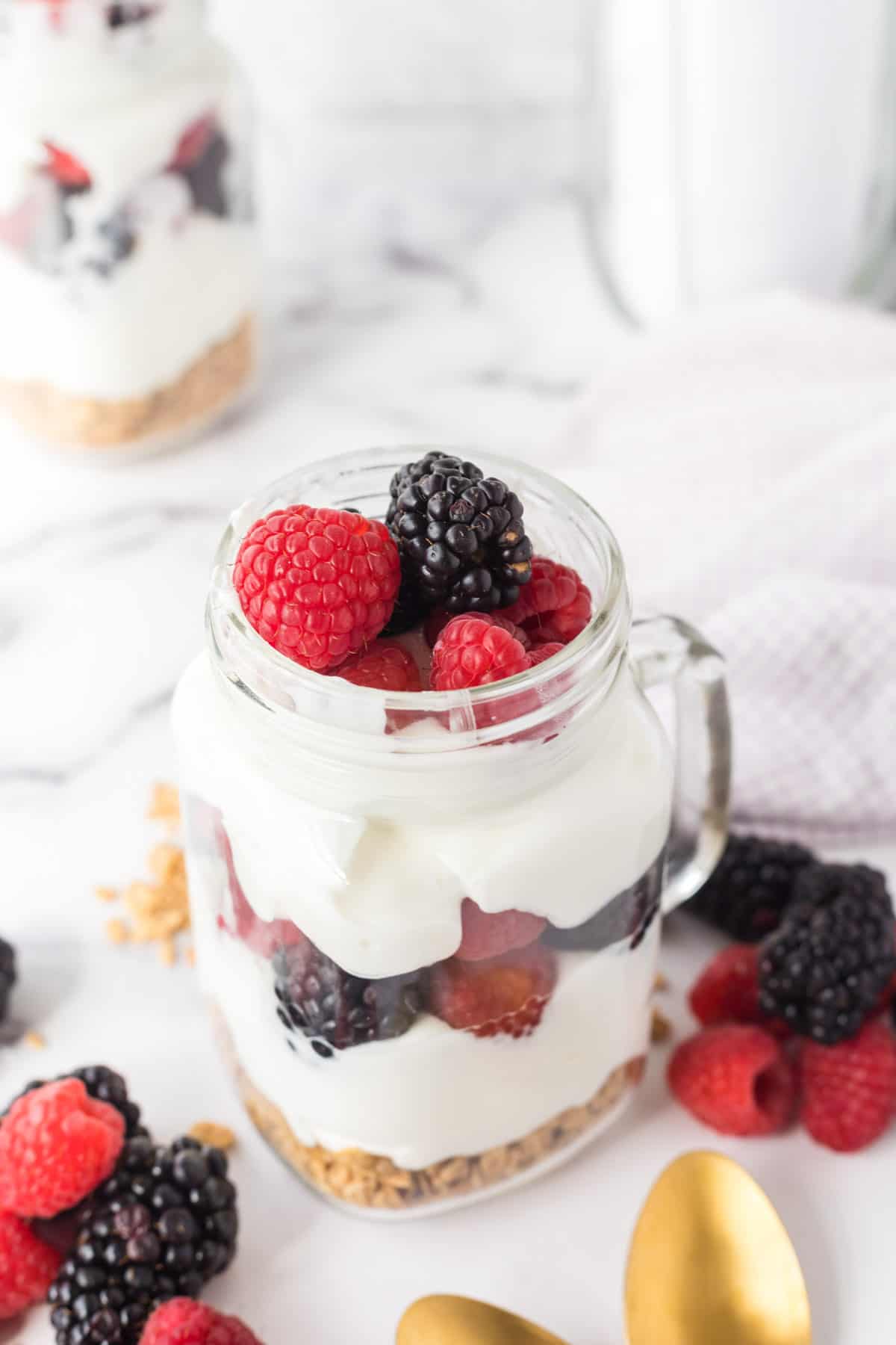 A Mason jar mug filled with a breakfast parfait made with granola, yogurt,, and fresh fruit.