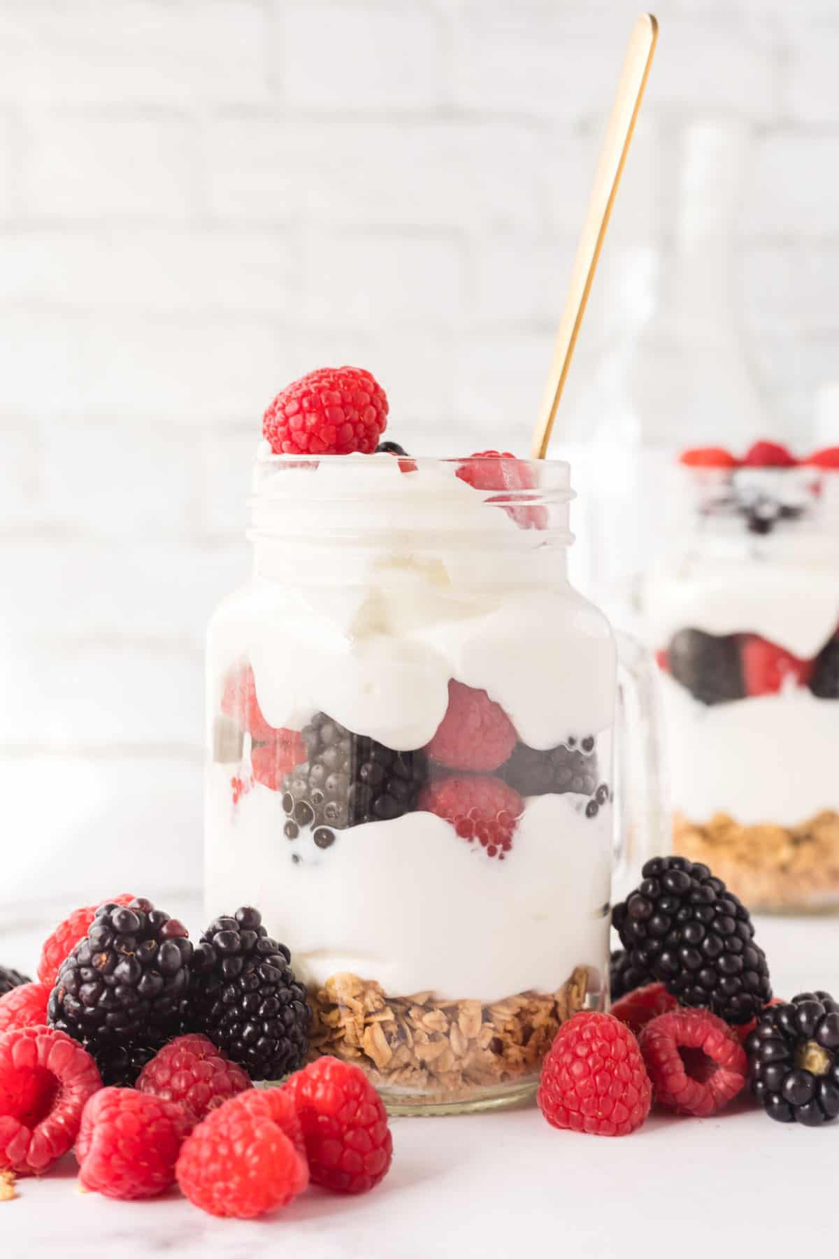 A glass jar filled with berry, yogurt, and granola parfait.