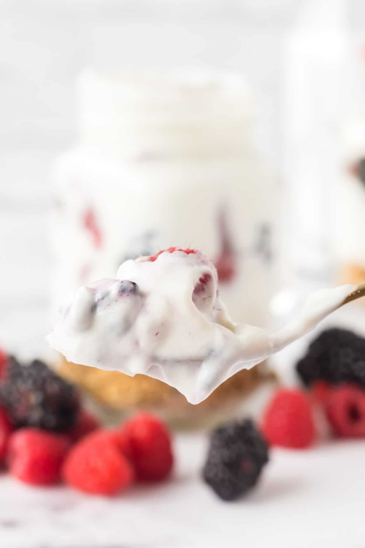 A spoonful with yogurt and berries ready for a bite to be taken.