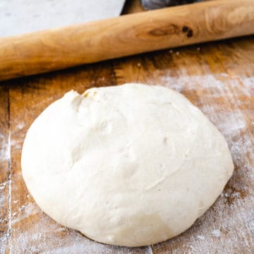 A no-rise pizza dough ball set on a floured wooden board.