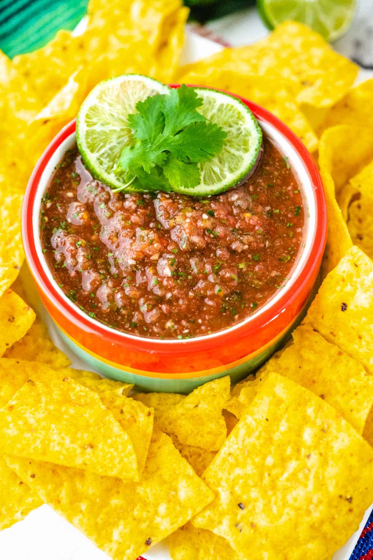 A colorful bowl of copycat Chili's salsa garnished with lime slices and cilantro with tortilla chips around the bowl.