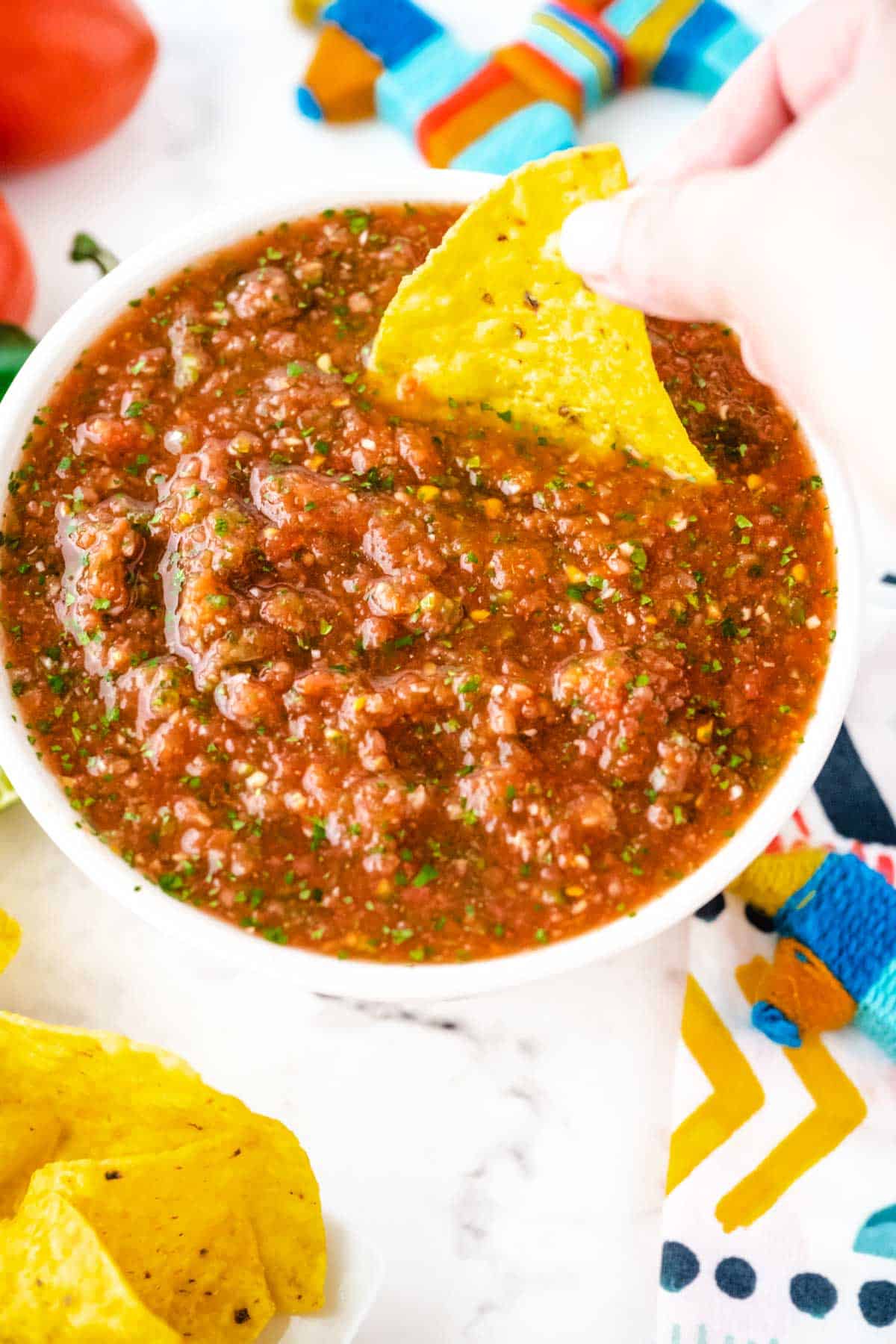 A white bowl of salsa with a hand dipping a tortilla chip into the salsa.