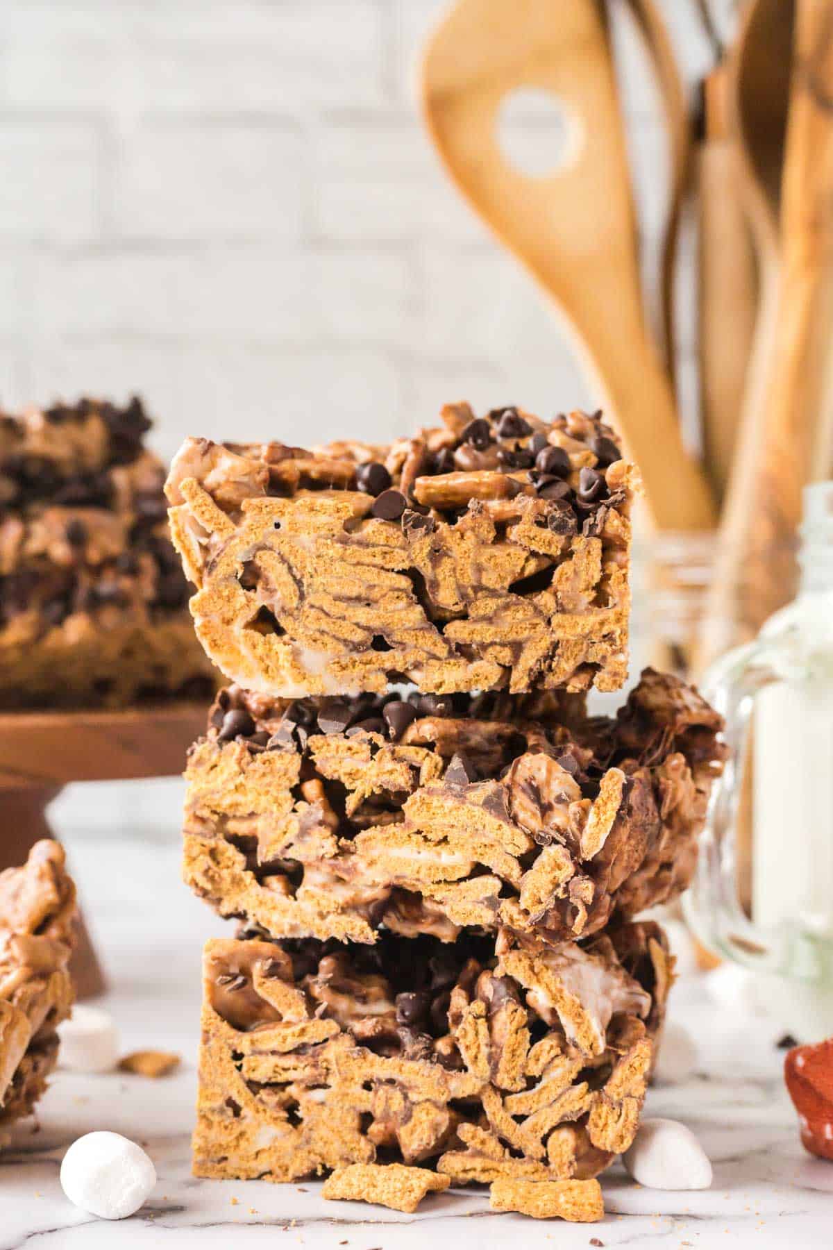 S'mores cereal bars stacked three high on a marble counter with wooden kitchen spoons in the background.