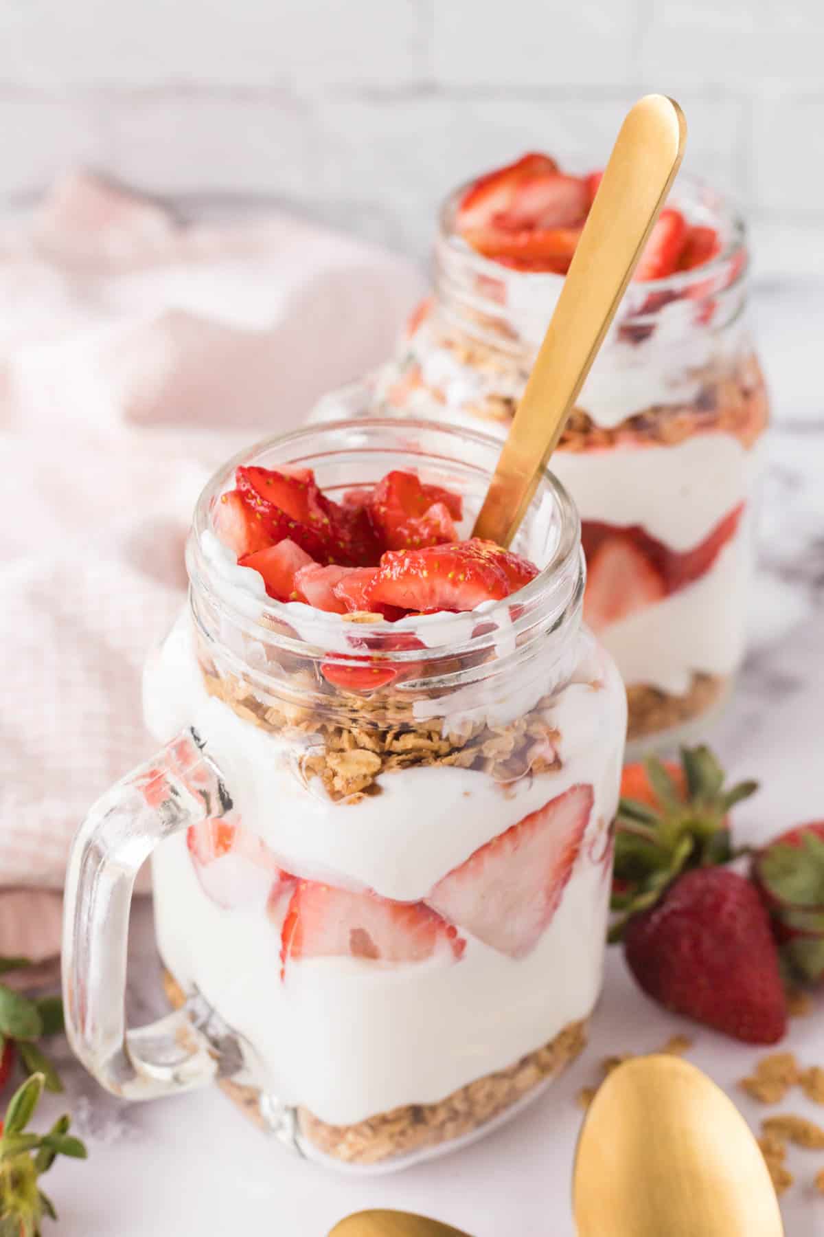 A mason jar mug with strawberry breakfast parfait with a gold spoon.