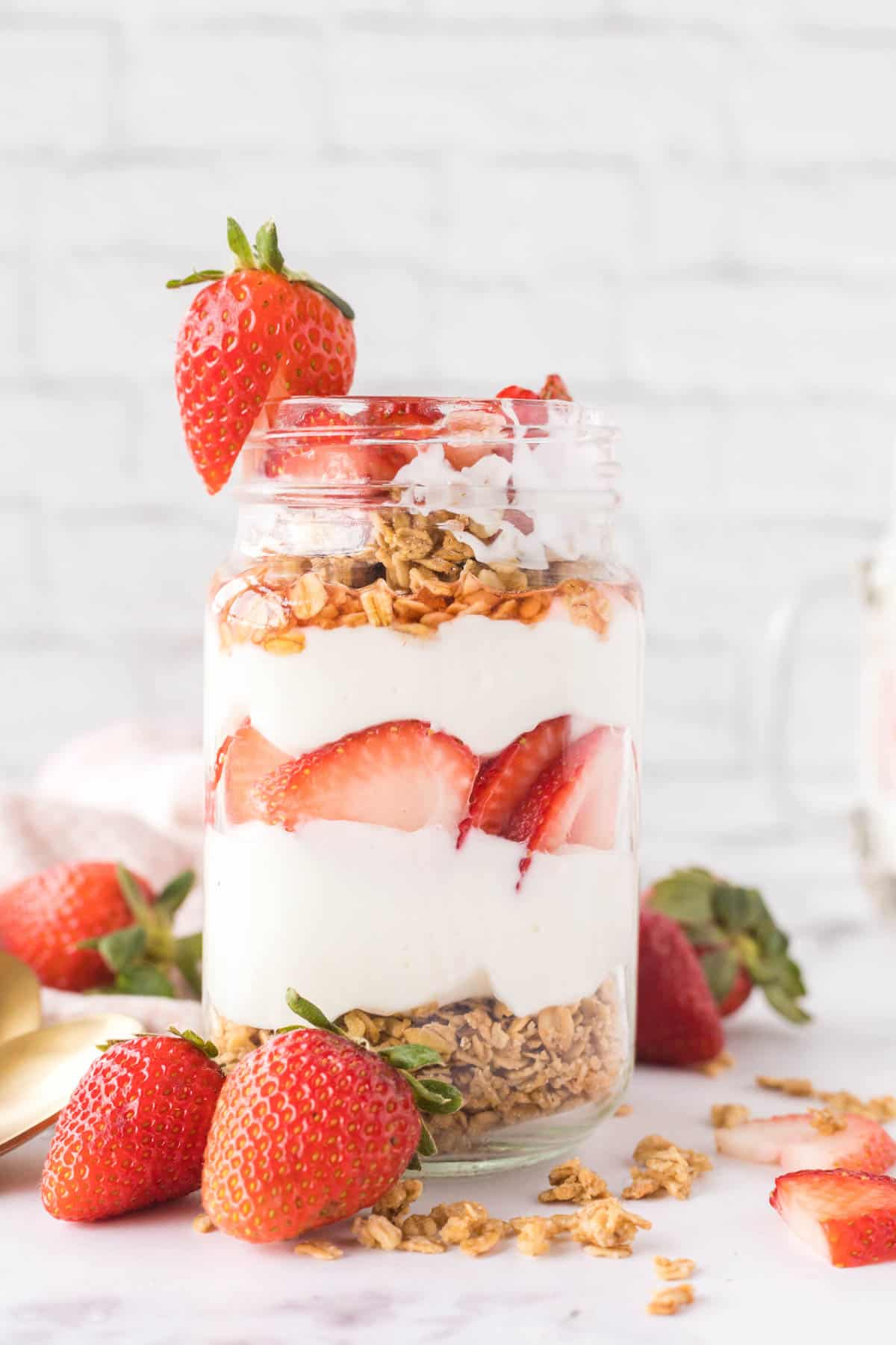 A strawberry granola parfait in a mason jar garnished with a whole strawberry on the rim.