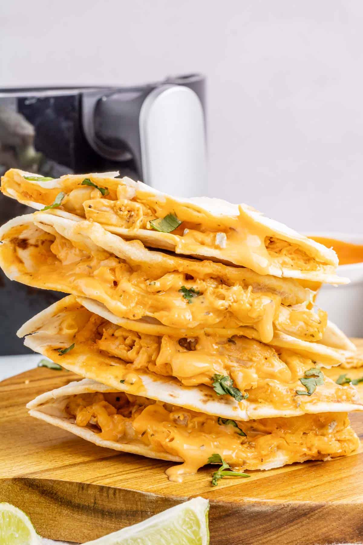 Quesadilla triangles stacked on top of each other with gooey cheese and buffalo sauce oozing out.