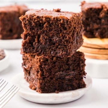 A small white wooden plate filled with two sliced brownies stacked on top of each other with a spoon to the side.