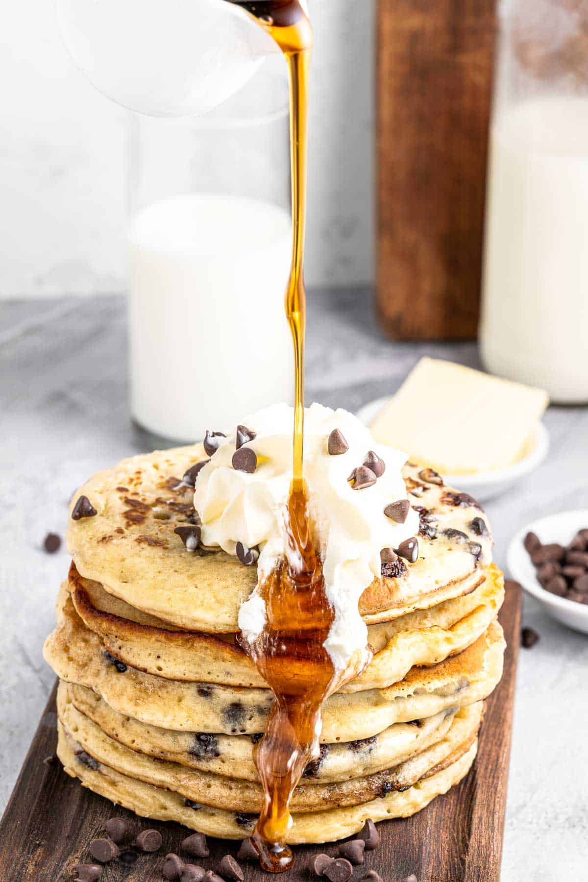 A stack of chocolate chip pancakes with syrup being poured on top.