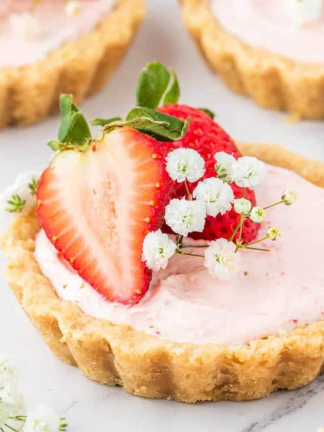 A mini strawberry tart set on a white marble table decorated with baby breath and strawberries.