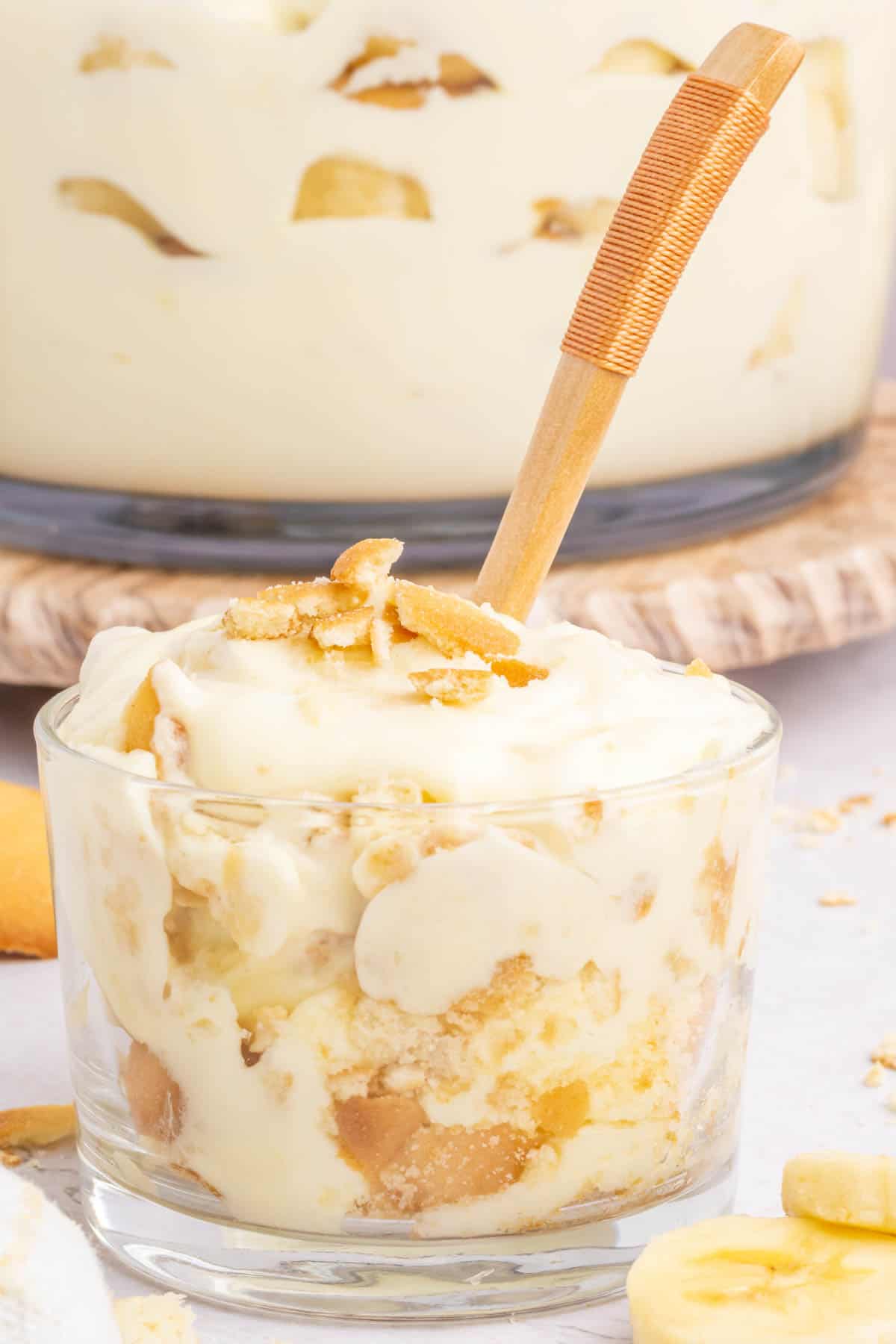 A clear dessert cup filled with banana pudding with a wooden spoon in it.