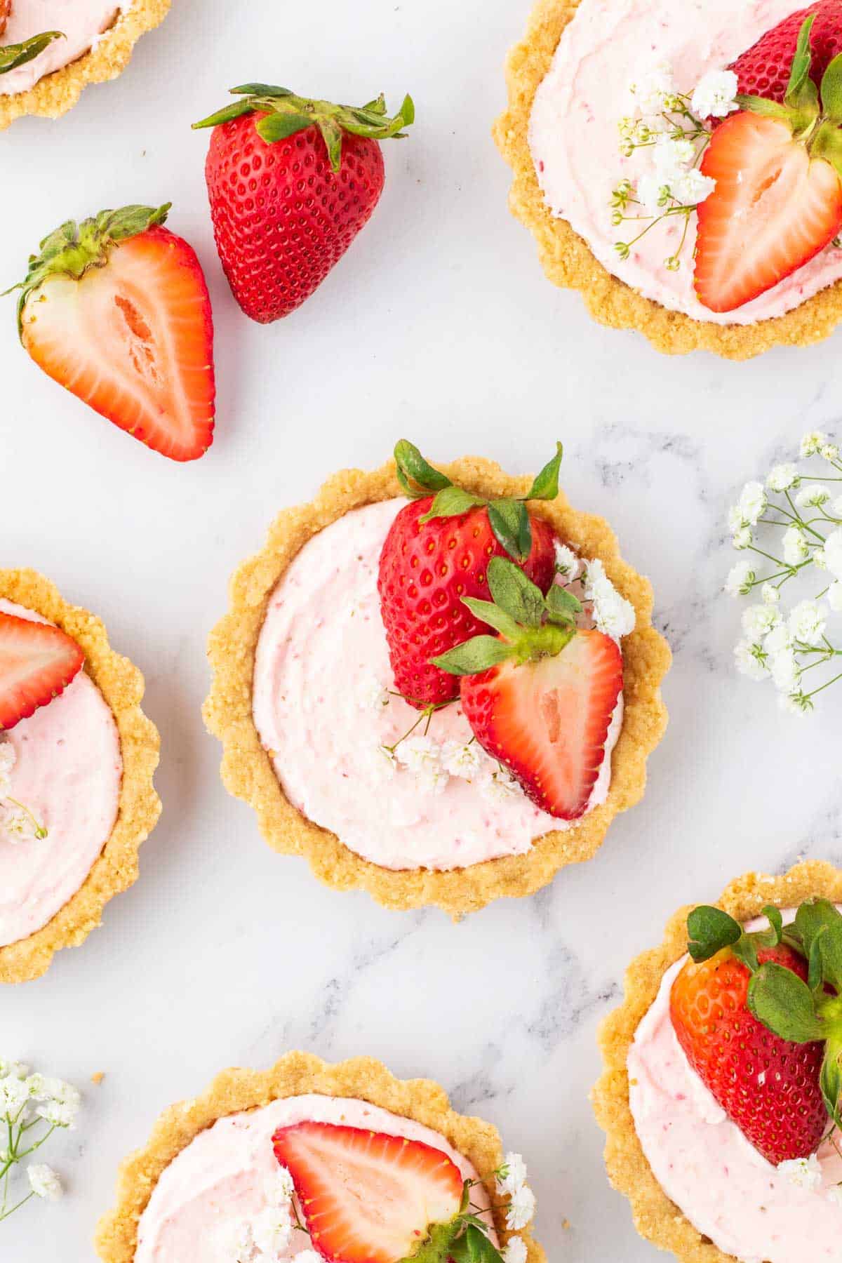 Mini strawberry tartlet garnished with halved strawberries and babies breath on a marble table.