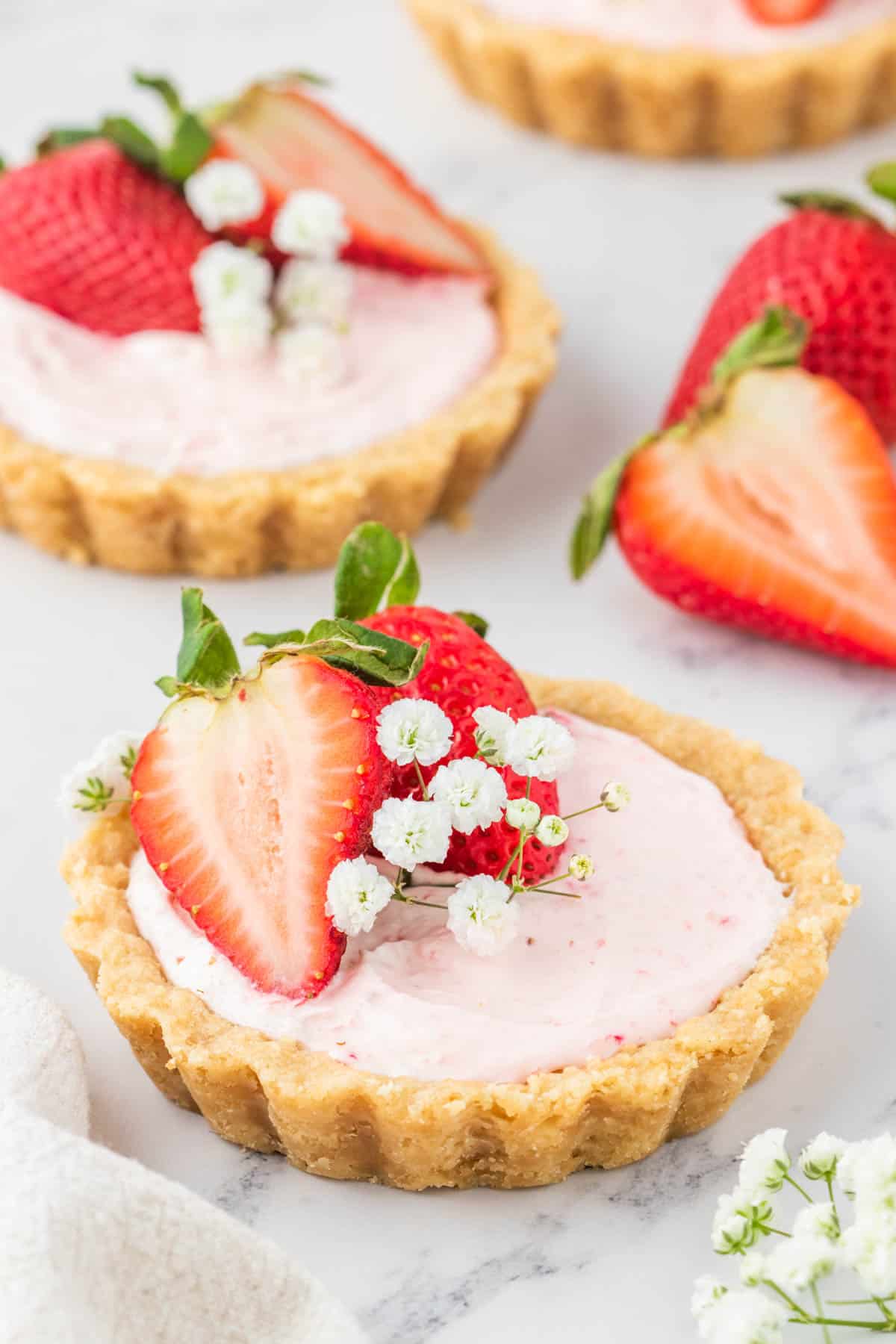 A mini strawberry tart set on a white marble table decorated with baby breath and strawberries.