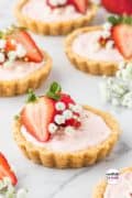 A close-up photo of mini strawberry tartlets with golden Oreo shells, filled with creamy strawberry filling and topped with fresh strawberries.