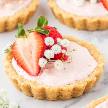 A mini strawberry tart set on a white marble table decorated with baby breath and strawberries.