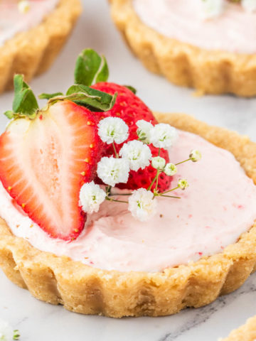 A mini strawberry tart set on a white marble table decorated with baby breath and strawberries.