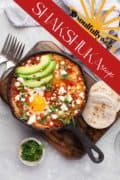 Labeled Pinterest image with shakshuka eggs in a skillet set on a wooden tray.