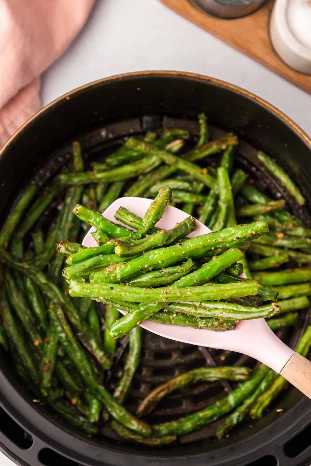 Cooked air fryer greens beans being scooped out with a wooden spoon.