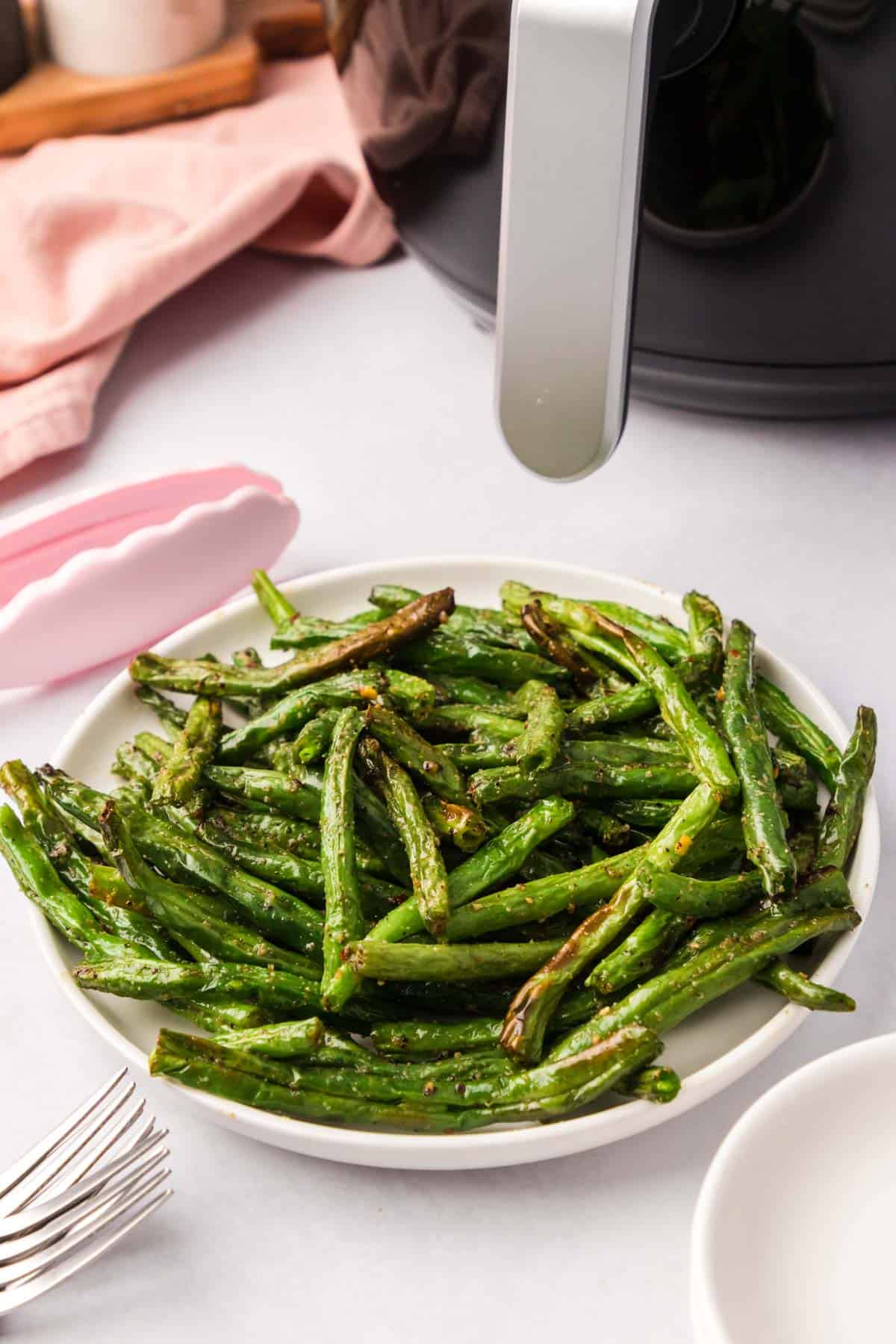 A plate of green beans with an air fryer in the background.