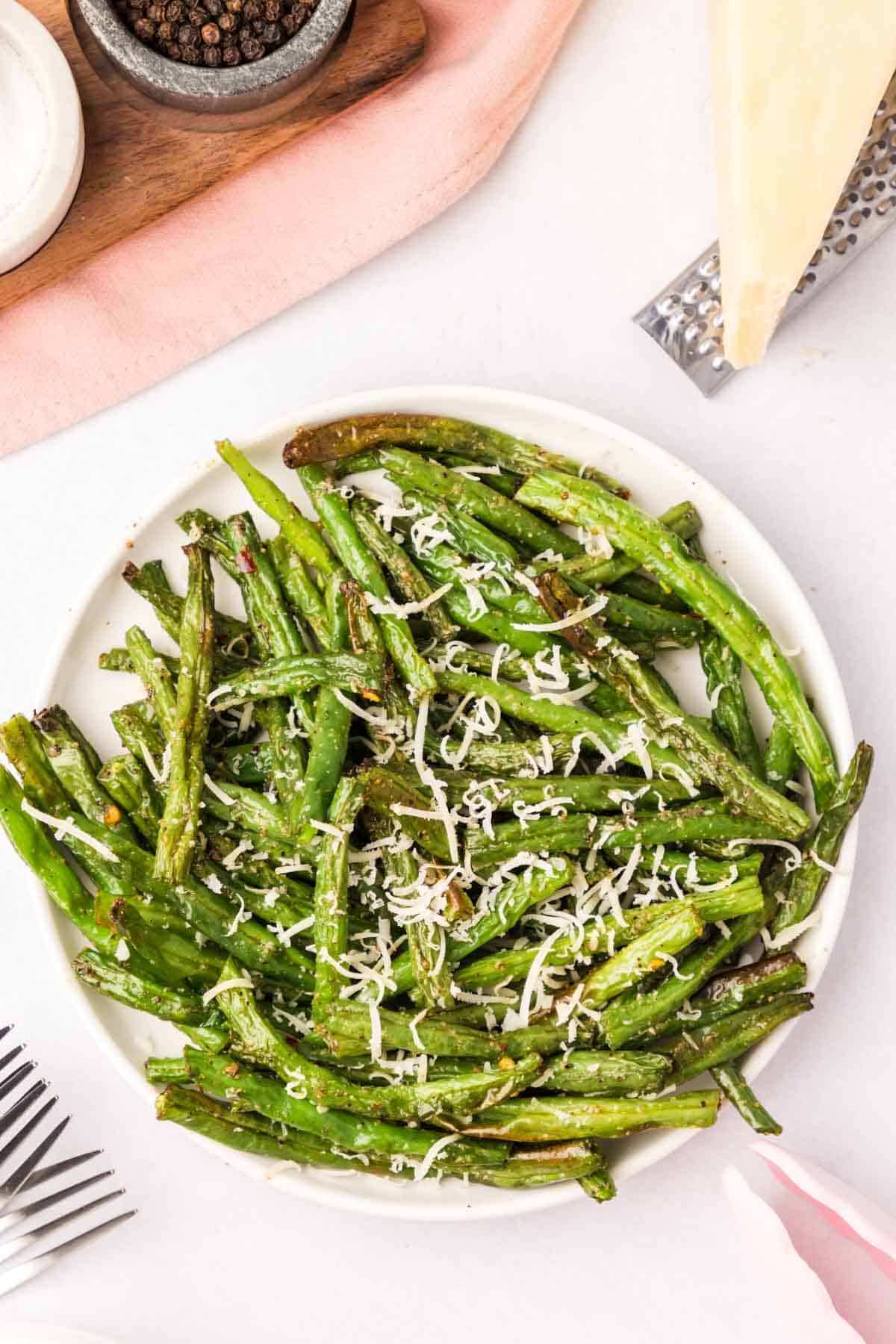 Air fryer green beans on a white plate garnished with fresh parmesan cheese.