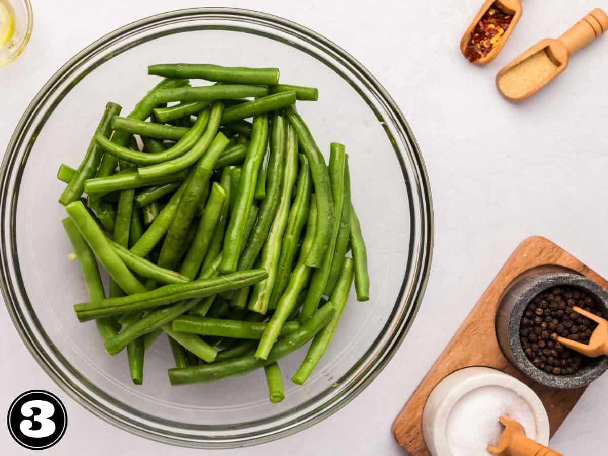 Green beans in a glass bowl drizzled with olive oil.