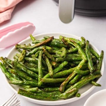 A plate of green beans with an air fryer in the background.