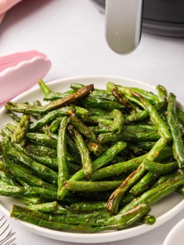 A plate of green beans with an air fryer in the background.