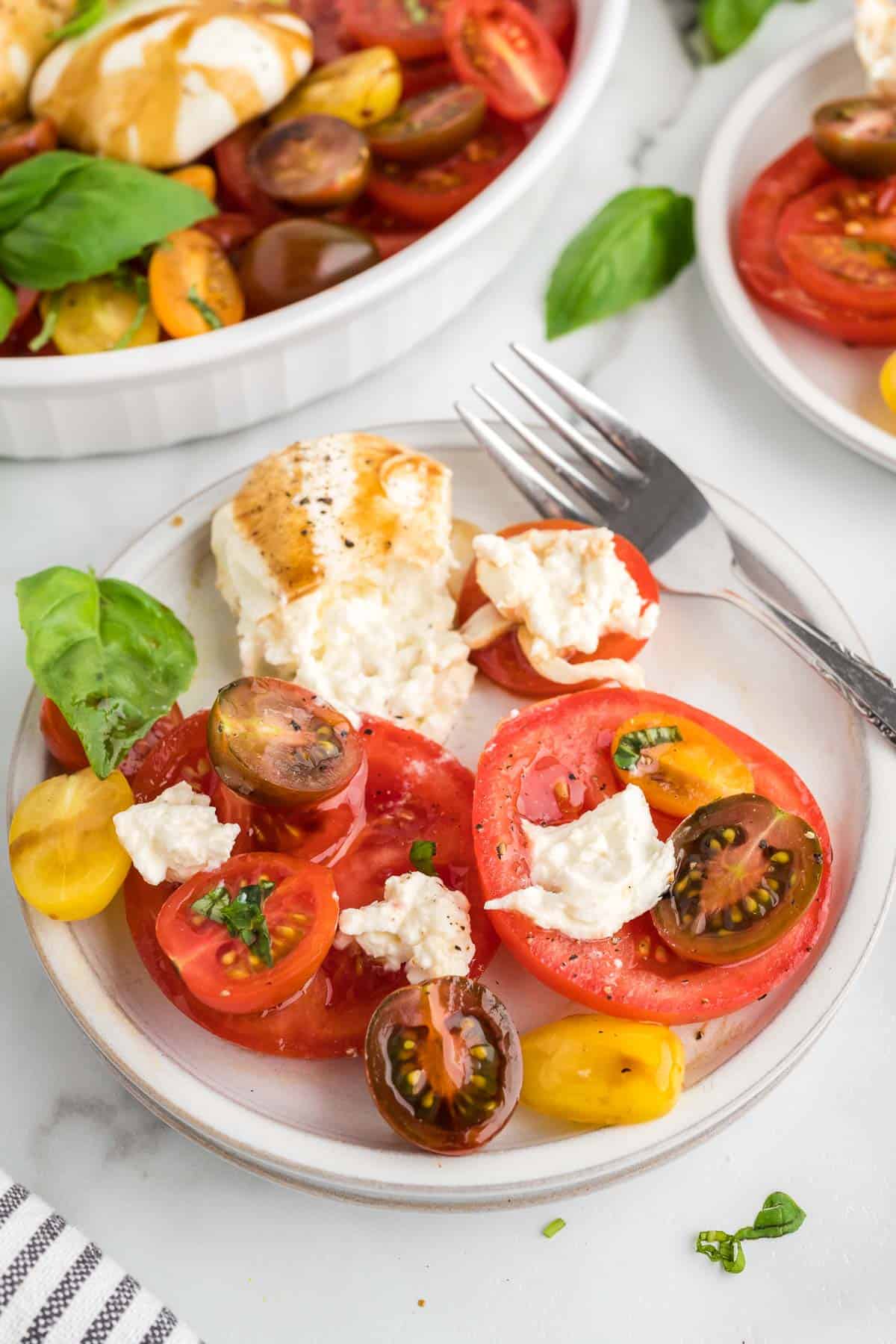 A white plate filled with a portion of burrata caprese salade.