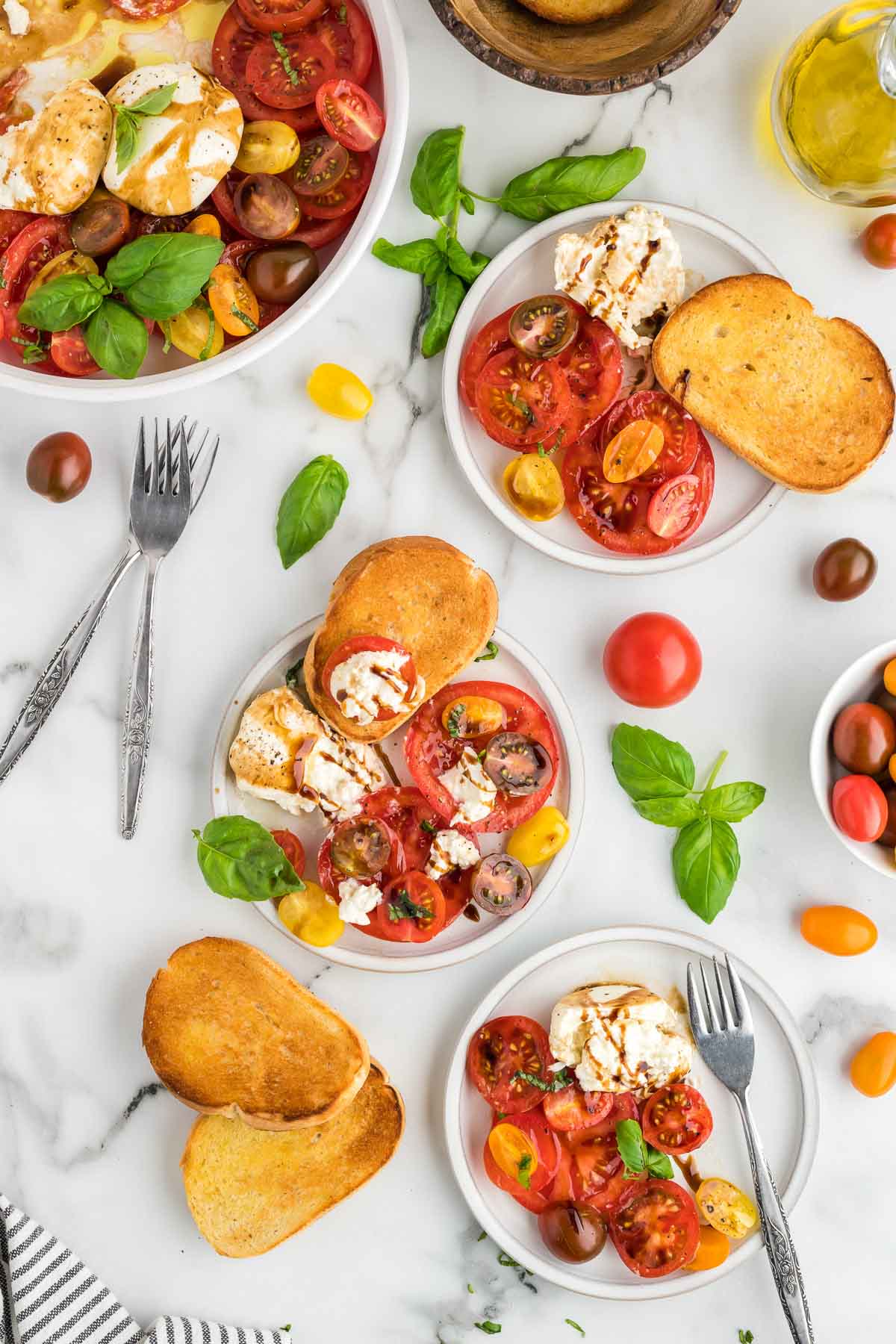 A table with plates of burrata caprese salad on serving plates and bread for serving.