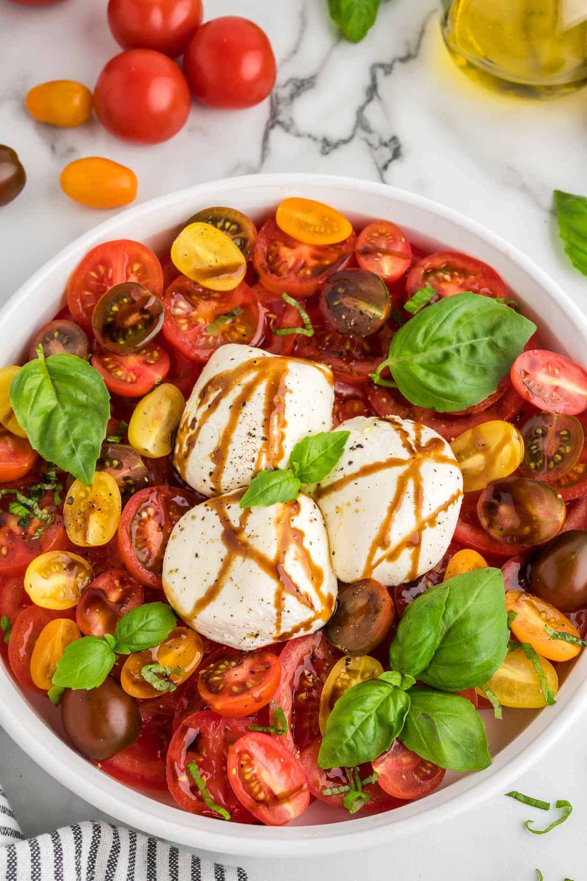 A white serving platter filled with sliced tomatoes, burrata cheese, balsamic glaze, and basil.